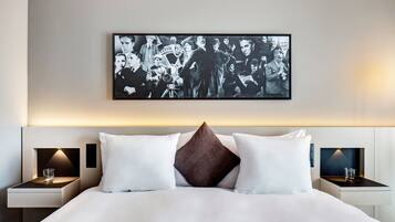 Une chambre d’hôtel avec un grand lit, deux tables de chevet avec des lampes et une photographie en noir et blanc encadrée accrochée au mur.