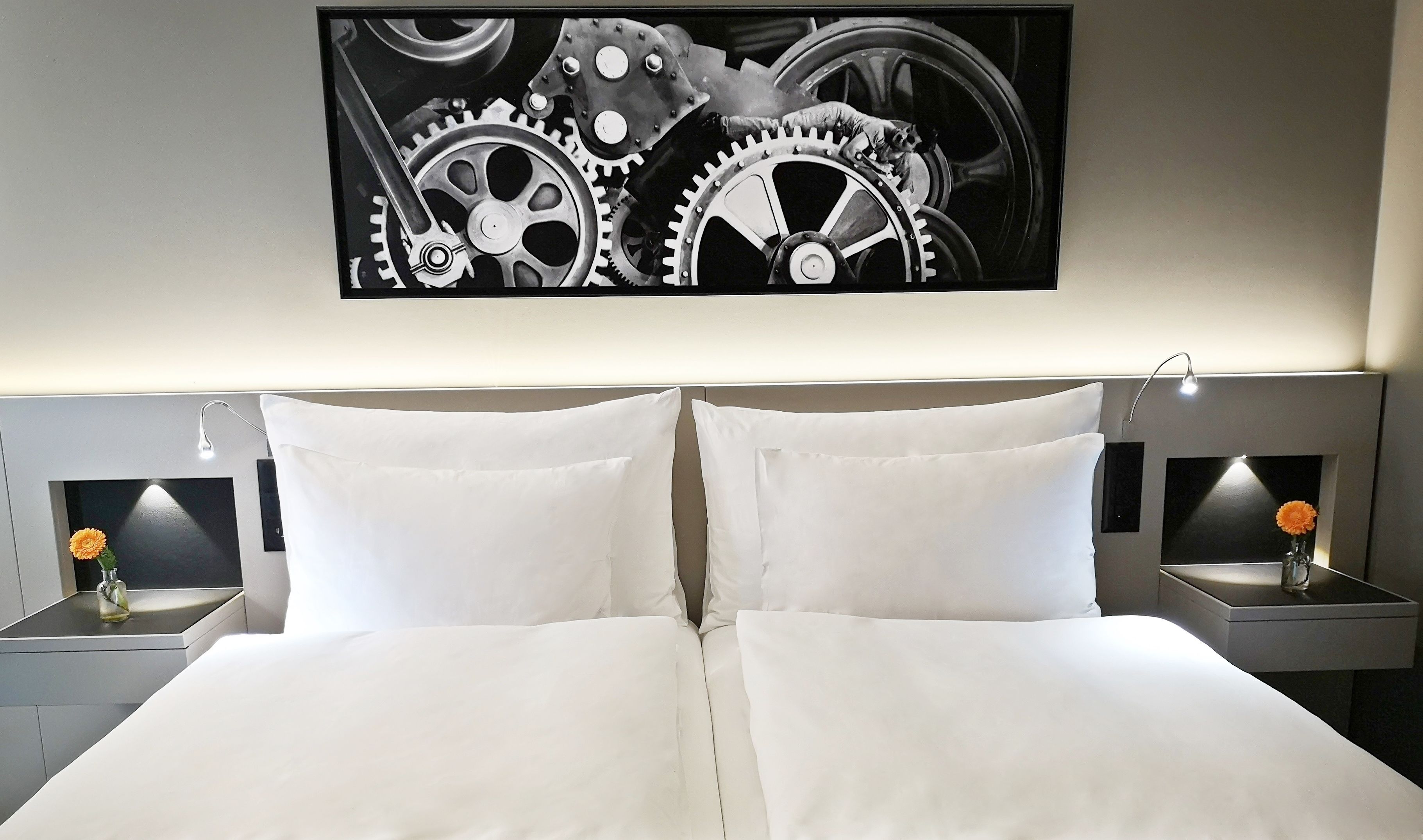 A neatly made bed with white linens, two bedside tables with lamps, and a large abstract painting above the bed.