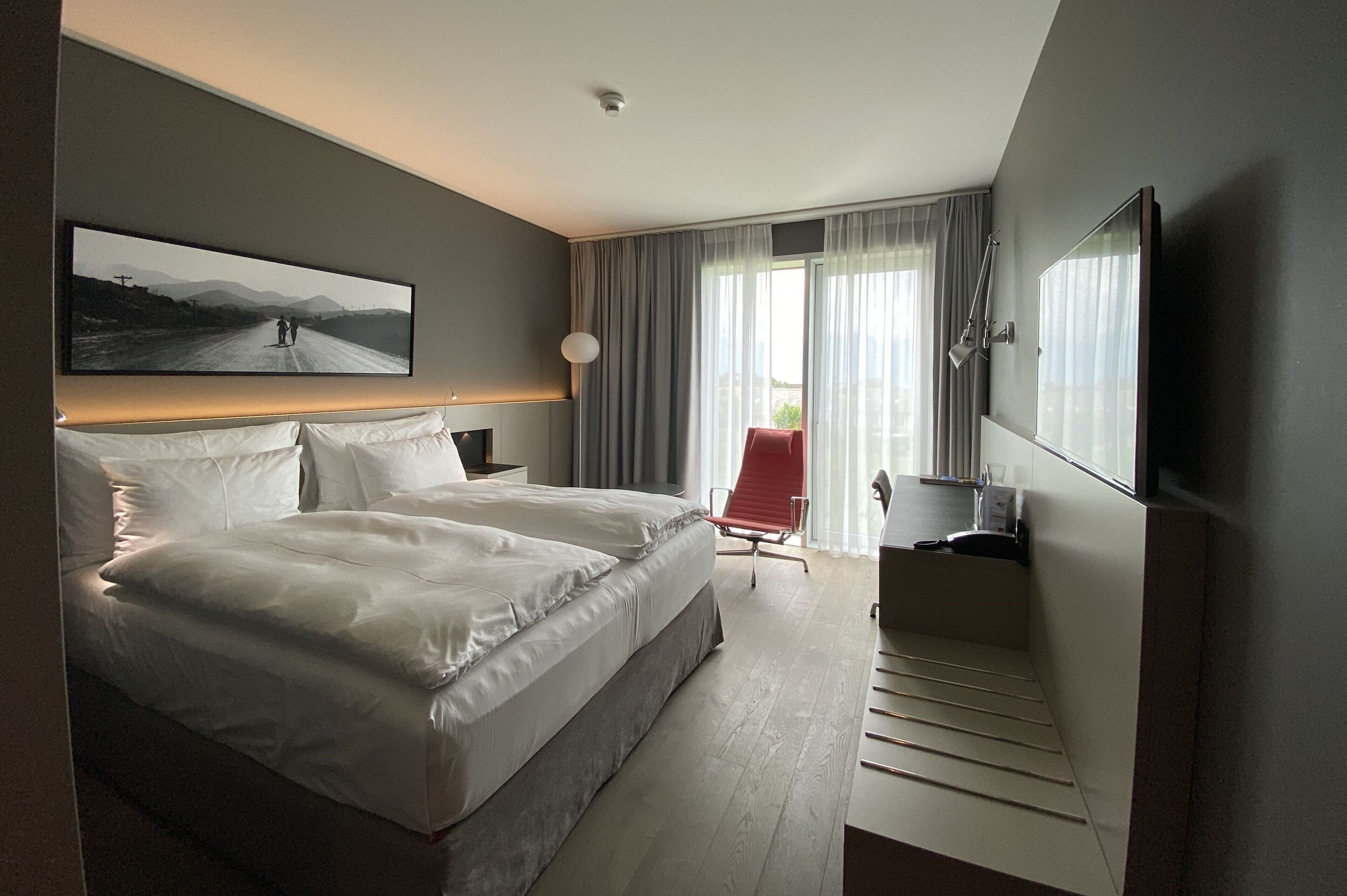 Et moderne hotelværelse med en stor seng, et fladskærms-TV, et skrivebord med stol og et vindue med gardiner.