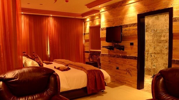 A bedroom with a bed, a TV mounted on the wall, and a door leading to a bathroom. - Jad Hotel Suites (Amman)