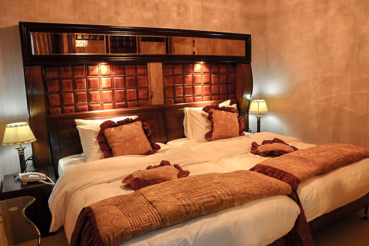 A hotel room with a large bed, two bedside tables, a nightstand, and a headboard with a wooden panel design.