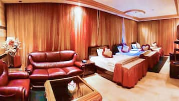 Habitación de hotel con un sofá de cuero grande, una cama con muchas almohadas, una mesita con un florero y un televisor.
