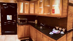 A compact kitchen with wooden cabinets, a microwave, a kettle, and a sink. - Jad Hotel Suites (Amman)
