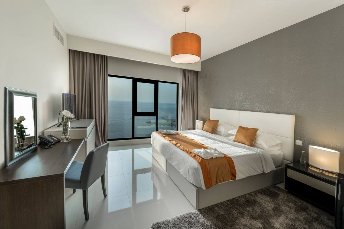 Une chambre d’hôtel moderne dotée d’un grand lit, d’un bureau, d’une chaise, d’une télévision et offrant une vue sur l’océan.
