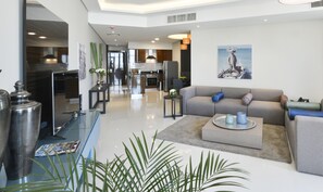 A modern living room with a grey sofa, a coffee table, and a kitchen in the background. - Lagoona Beach Luxury Resort and Spa (Budaiya)