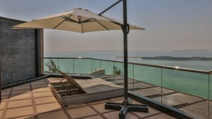 Un balcon avec vue sur la mer, un coin salon avec un transat et un grand parasol.