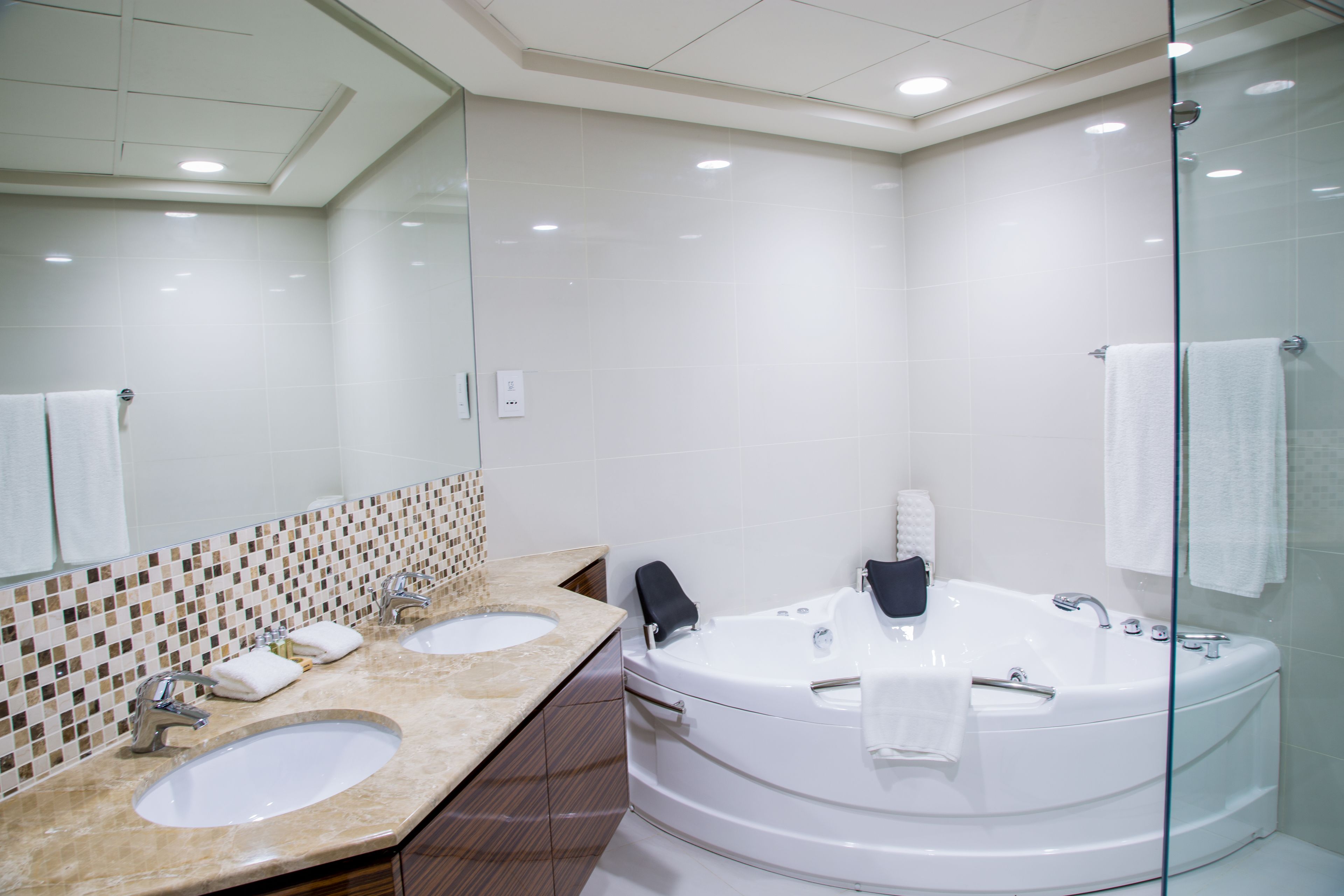 Un baño moderno con dos lavamanos, una bañera grande y un box de ducha de vidrio.
