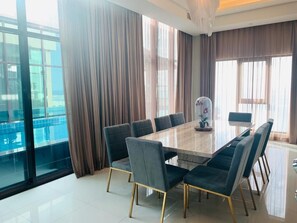A modern dining area with a large rectangular table, dark upholstered chairs, and a view through large windows. - Lagoona Beach Luxury Resort and Spa (Budaiya)