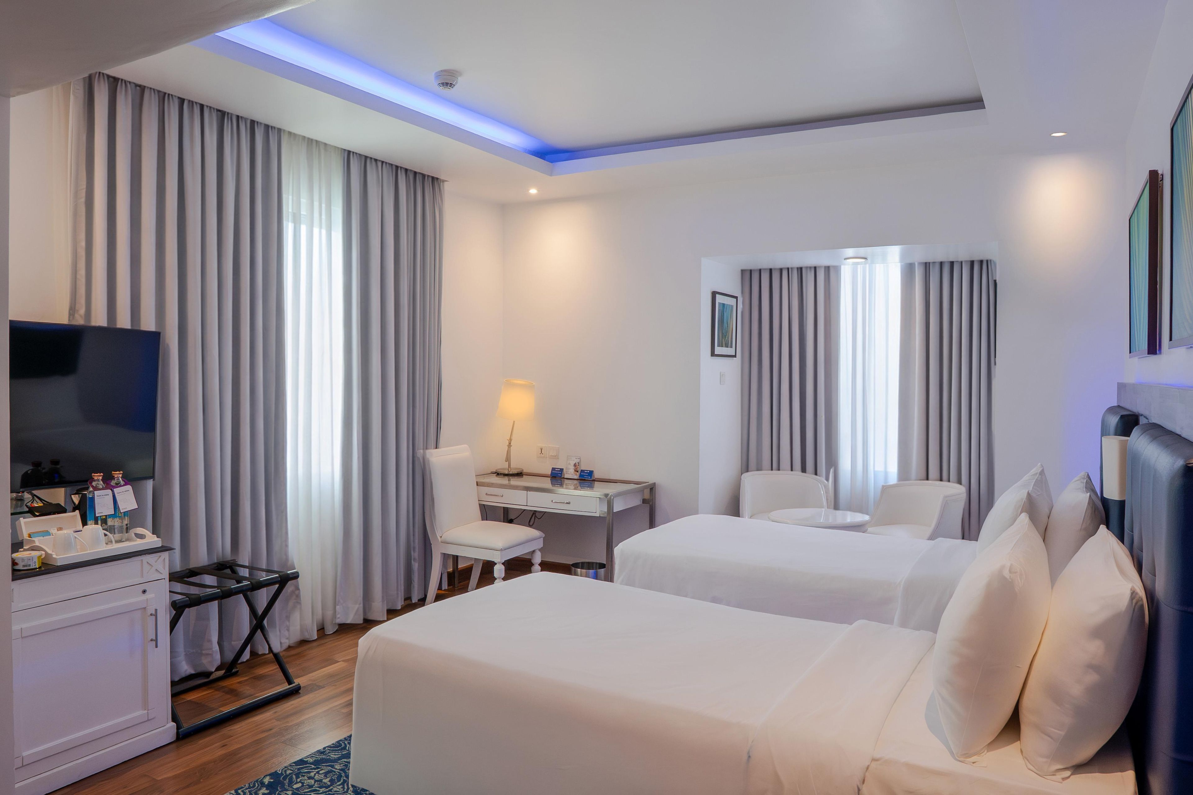 A hotel room with two beds, a desk, a chair, a TV, and a minibar.