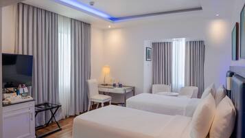 A hotel room with two beds, a desk, a chair, a TV, and a minibar.