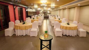 A banquet hall with round tables, white chairs, and chandeliers.