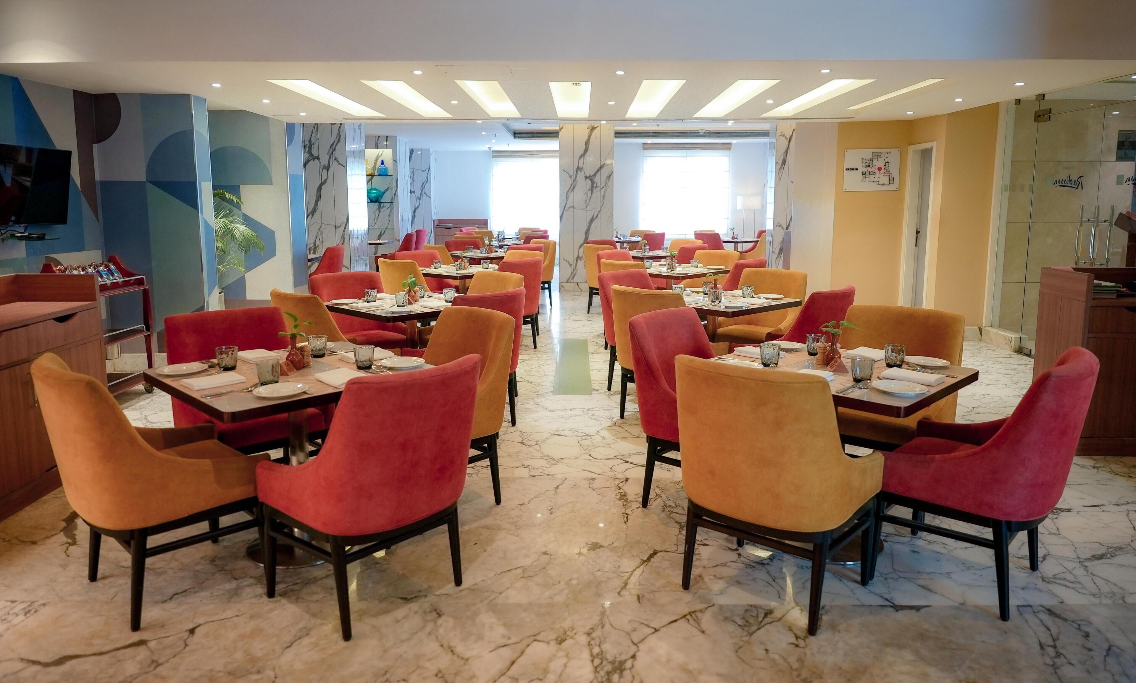Un restaurante con sillas rojas y anaranjadas, suelo de mármol y un diseño de techo moderno.