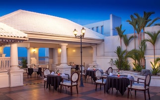 An outdoor dining area with tables and chairs, a covered section with columns, and a view of the sky.