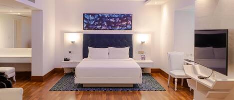Una habitación de hotel moderna con una cama grande, mesitas de noche, televisor, una silla y un espejo.