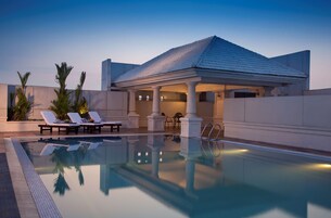 A pool area with lounge chairs and palm trees, a covered seating area, and a modern building with a tiled roof.