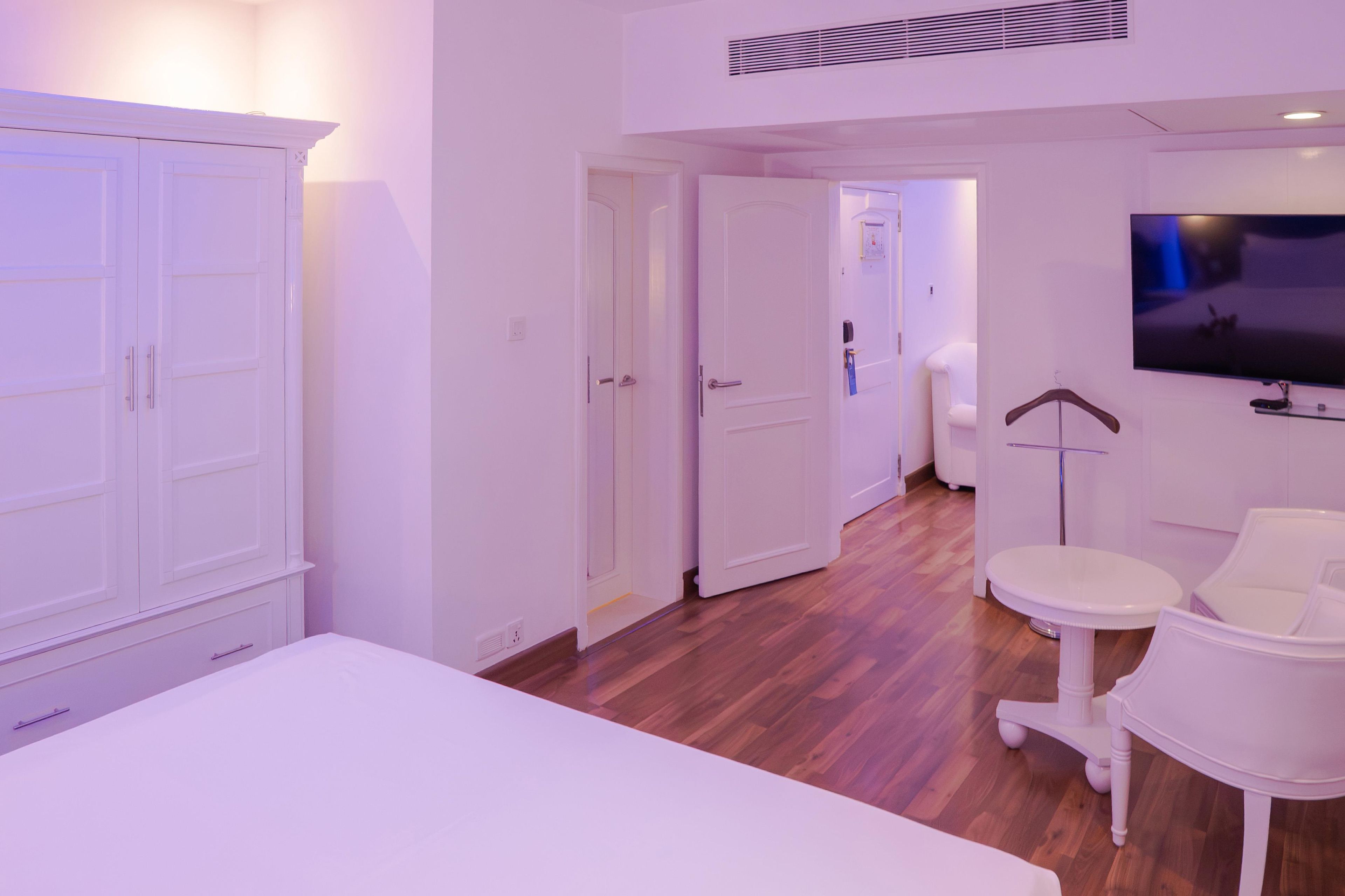 A hotel room with a bed, a TV, a desk, and a chair. There are doors leading to other rooms.