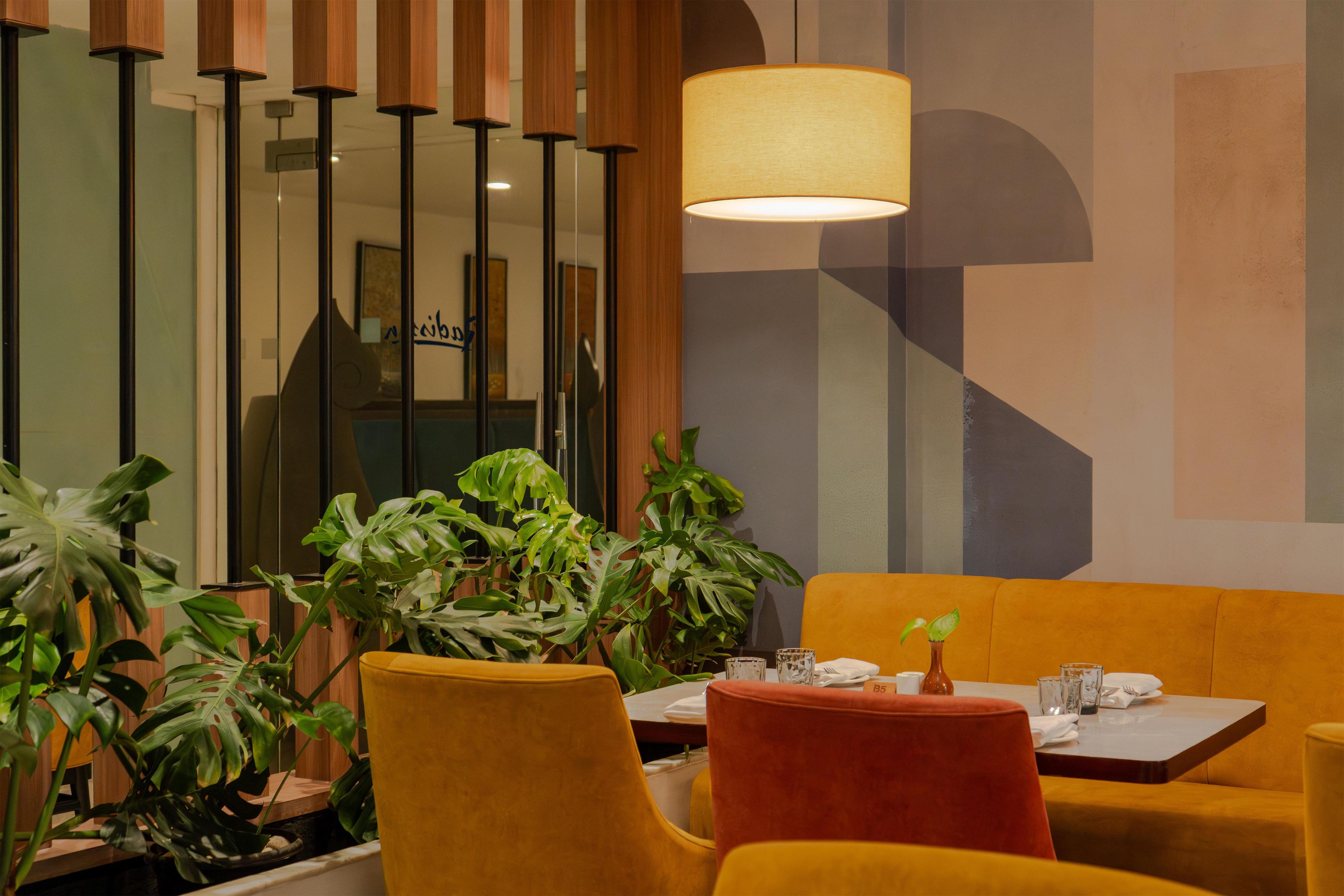 Um interior moderno com um sofá amarelo, uma mesa com um vaso e uma planta grande.