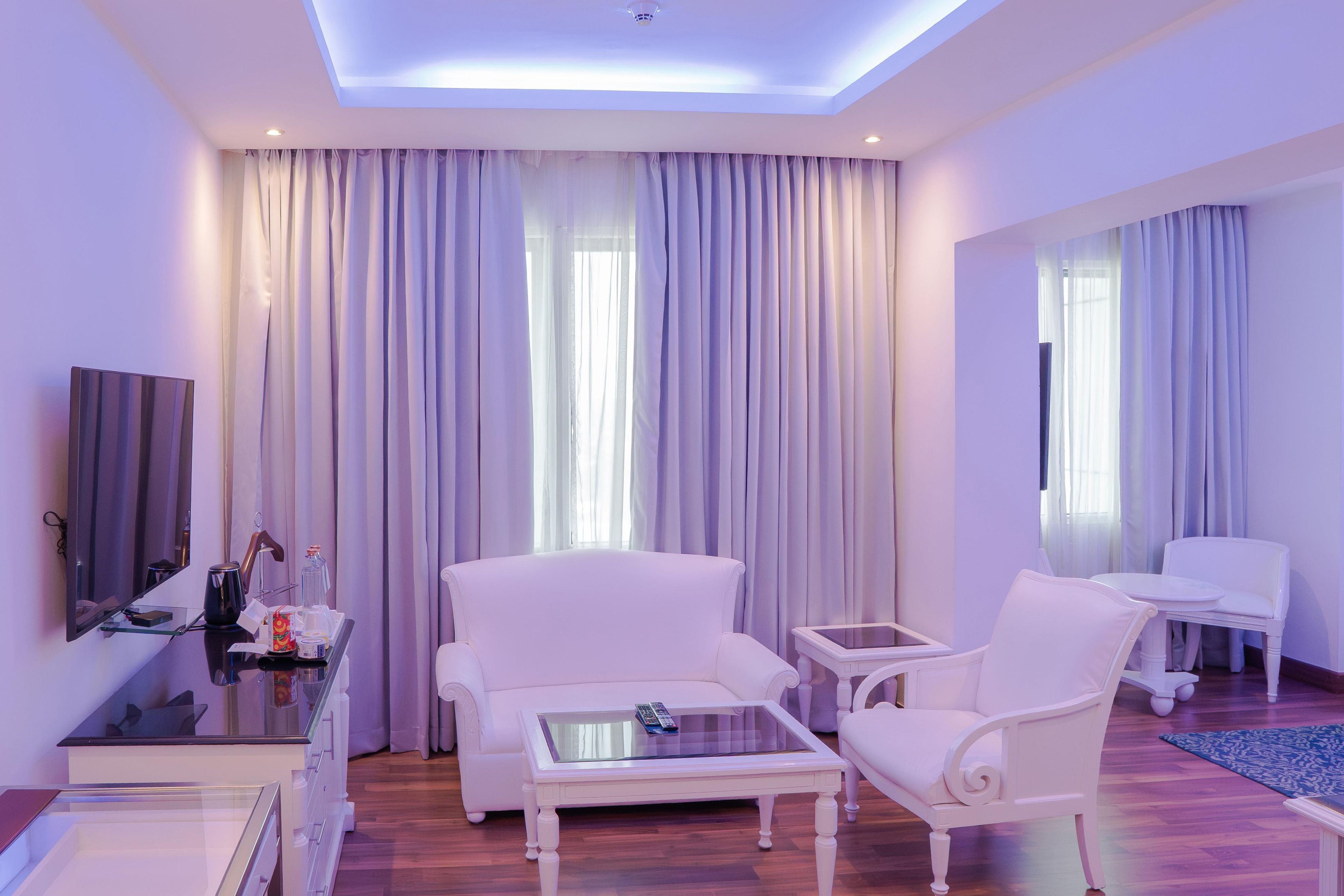 A modern hotel room with a sofa, a coffee table, a TV, and a desk with a mirror.