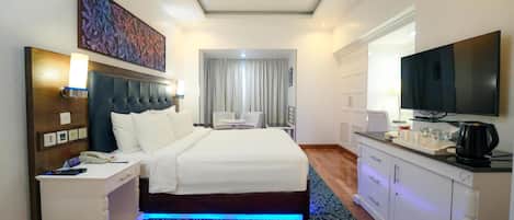 A hotel room with a bed, bedside table, lamp, TV, and a desk with a coffee maker.