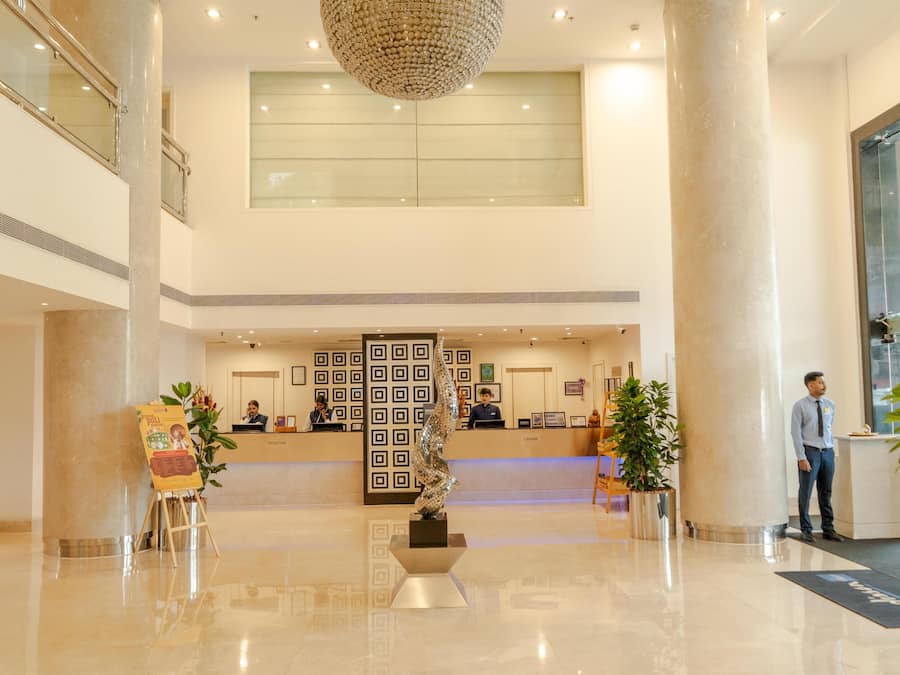 A hotel lobby with a reception desk, a large chandelier, and a modern design.