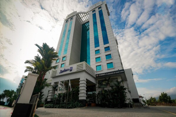 A modern hotel with a prominent entrance, a name sign, and a sign for 'ZHIMA FLAVOURS OF EAST ASIA'. - Radisson Blu Kochi (Kanayannur)