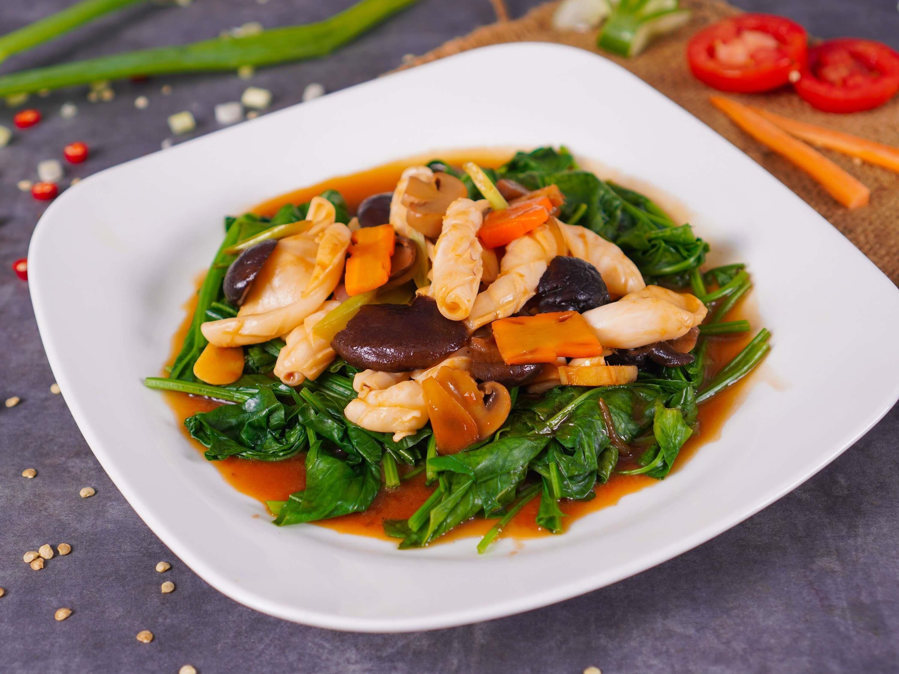 Un plato blanco con un salteado de verduras y camarones, adornado con semillas de sésamo.