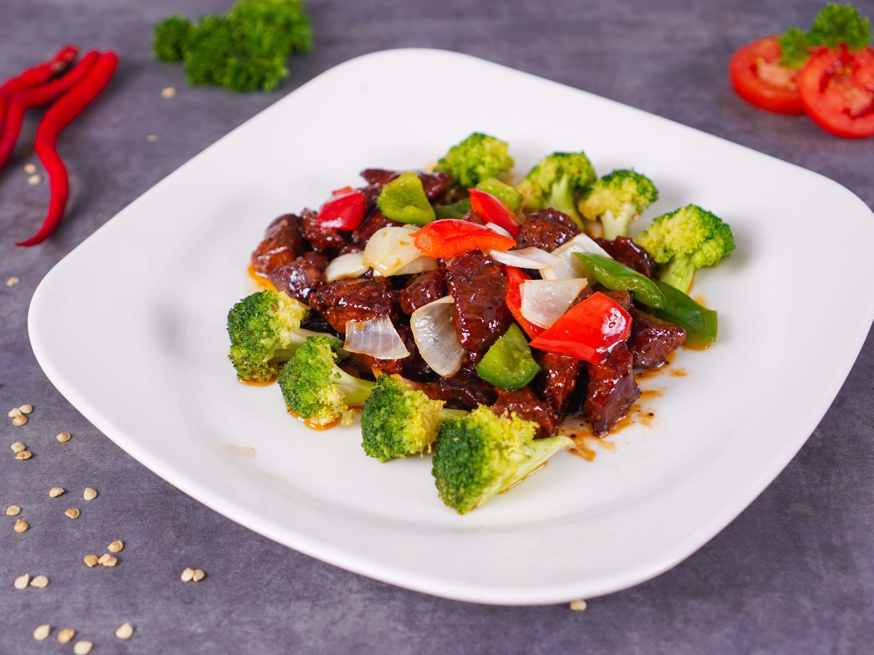 A white plate with a beef stir-fry dish, broccoli, and red bell peppers.