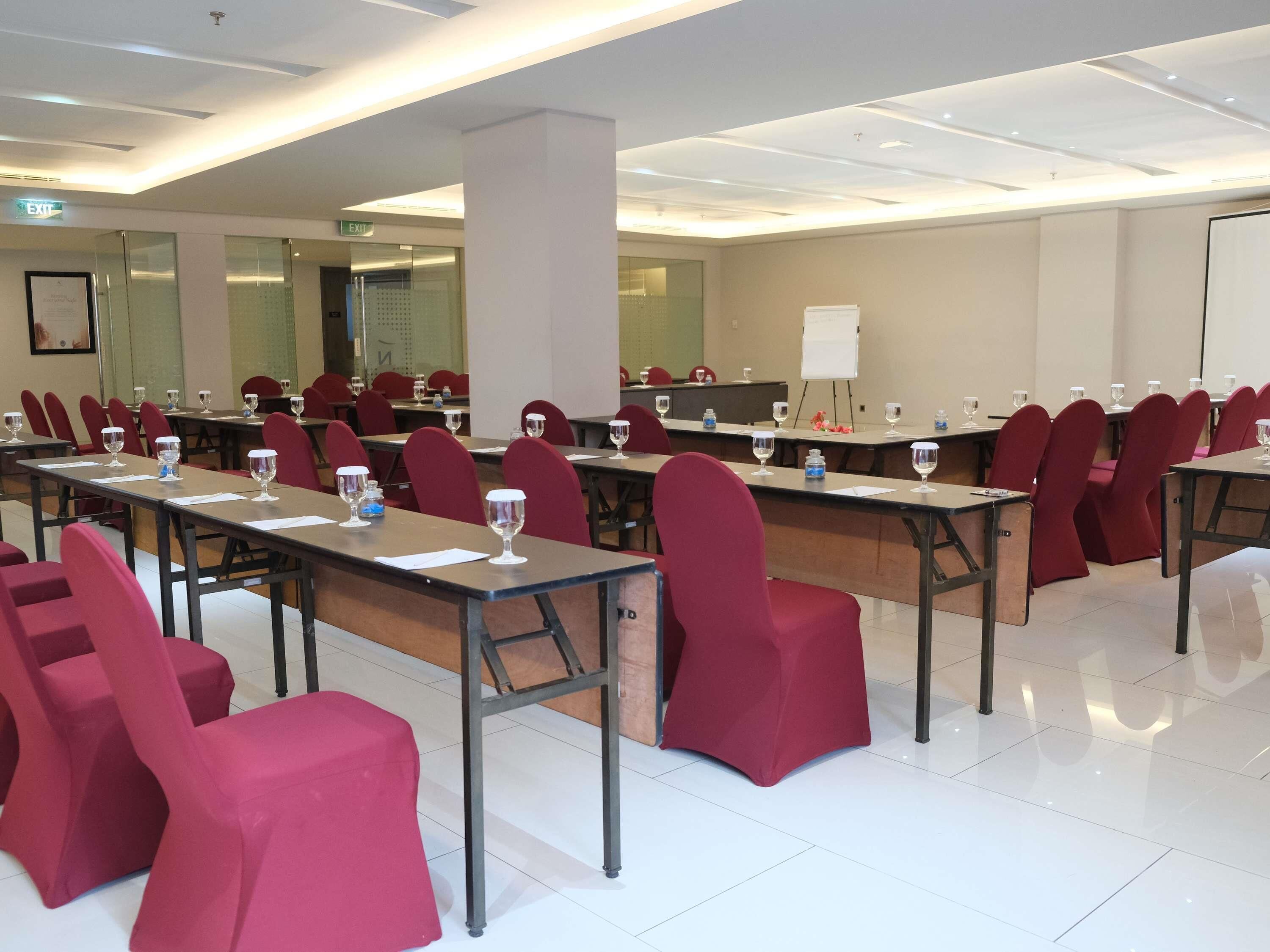 A conference room with rows of tables and chairs, a whiteboard, and an exit sign.