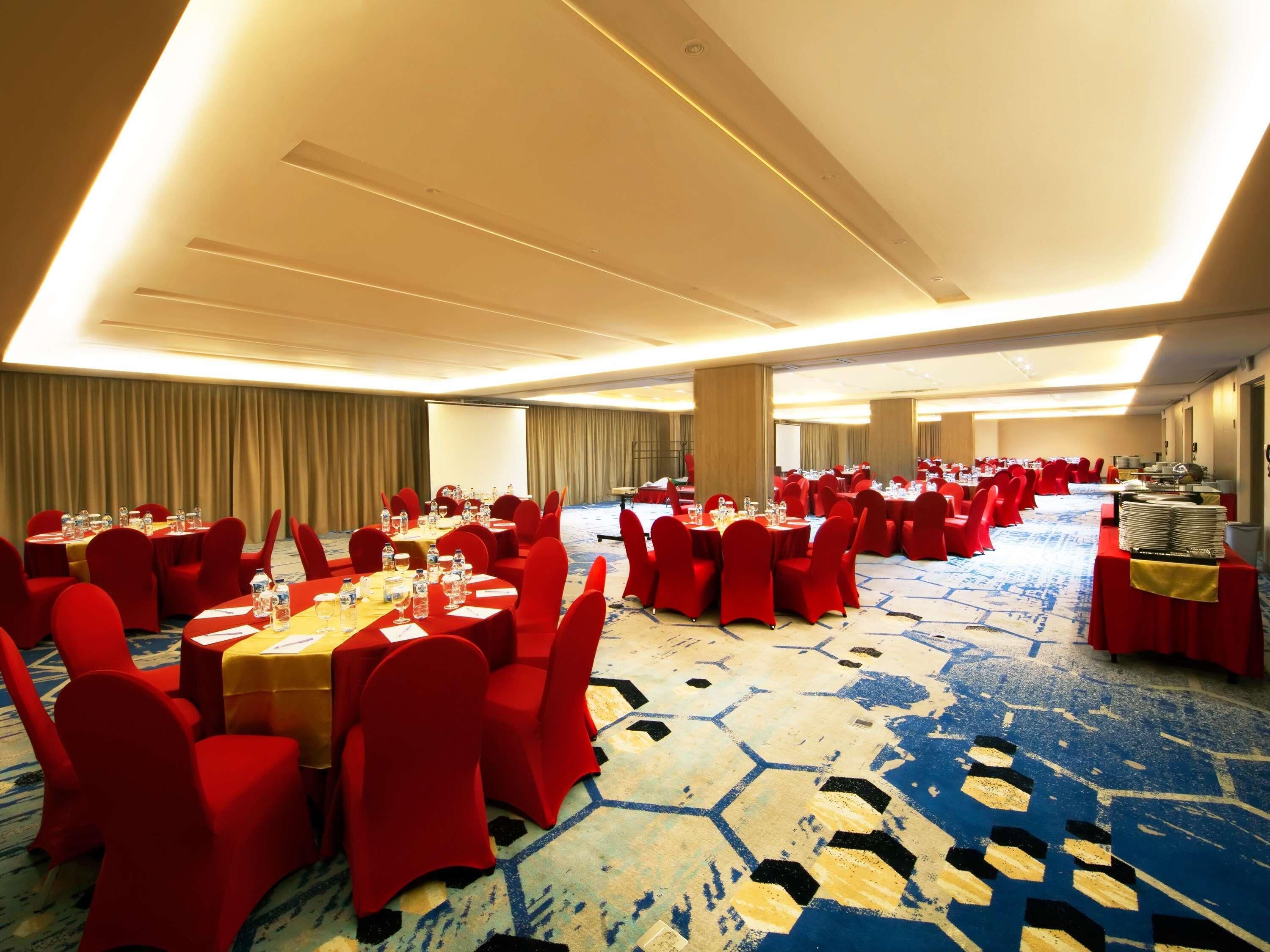 A large conference room with rows of tables and chairs, a carpeted floor, and a projector screen.