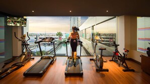 Une salle de sport équipée de tapis de course, de vélos d’appartement et dotée d’une grande fenêtre offrant une vue sur la ville.