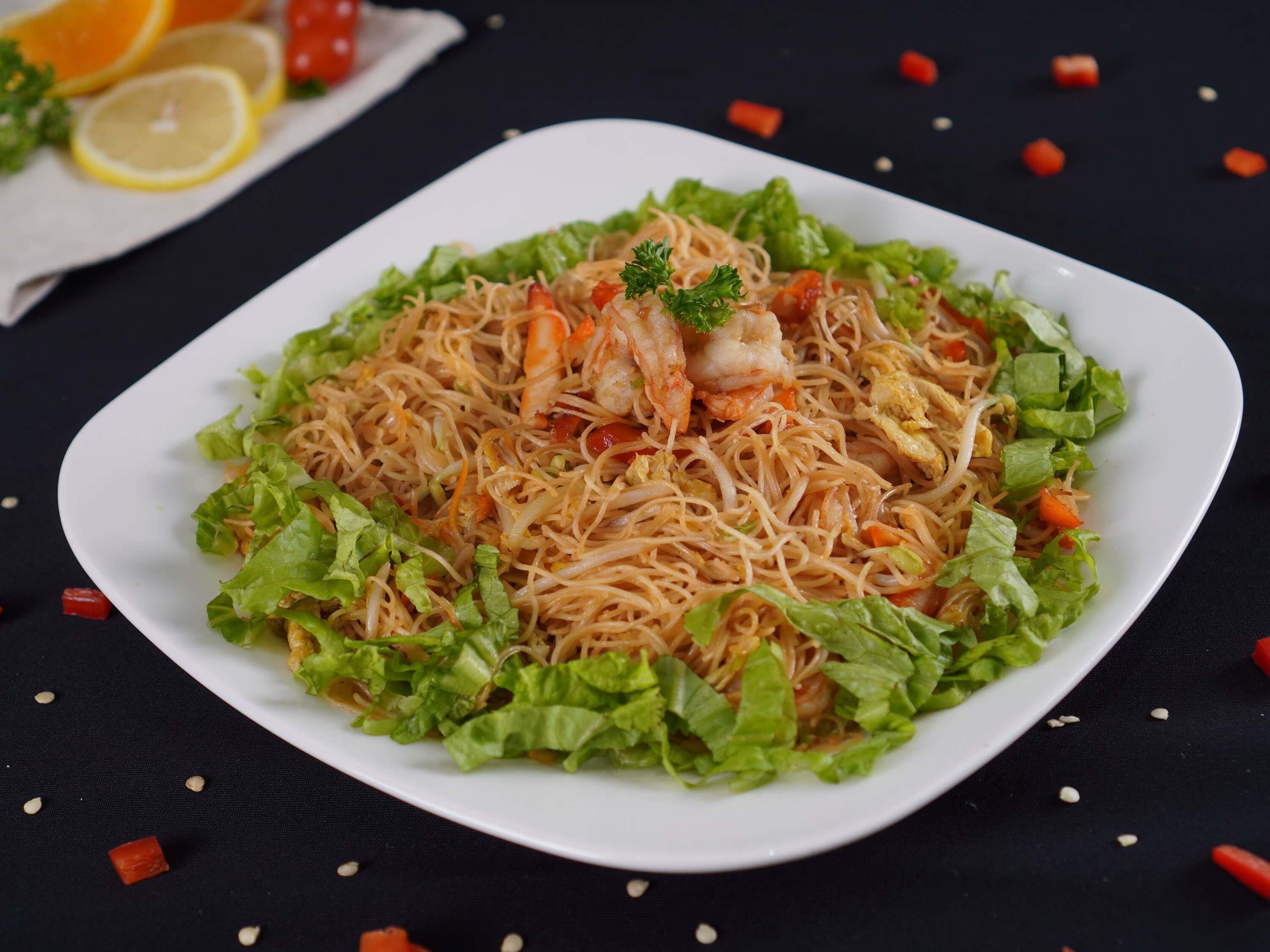 A plate of noodles with shrimp and vegetables on a white plate.