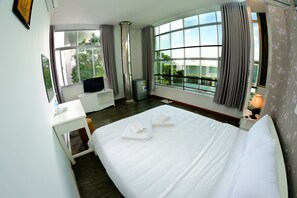 A hotel room with a large bed, a desk with a TV, a window with curtains, and a view of greenery outside. - Da Nang Center Hotel (Da Nang)