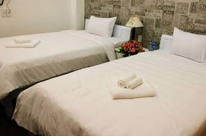 Two twin beds with white linens and towels, a nightstand with a lamp, and a wall with newspaper-style wallpaper. - Da Nang Center Hotel (Da Nang)