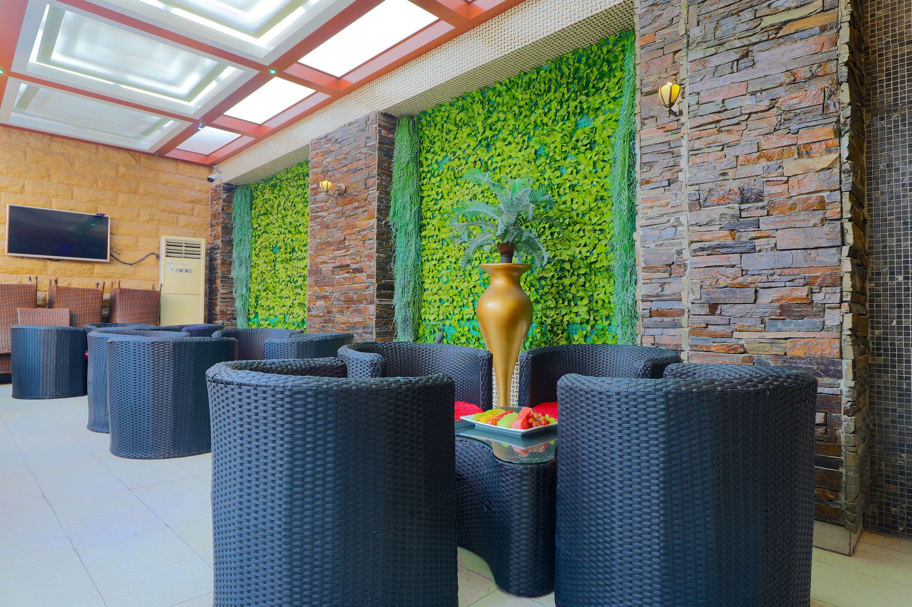 A lobby with wicker furniture, a large vase, and a green wall.