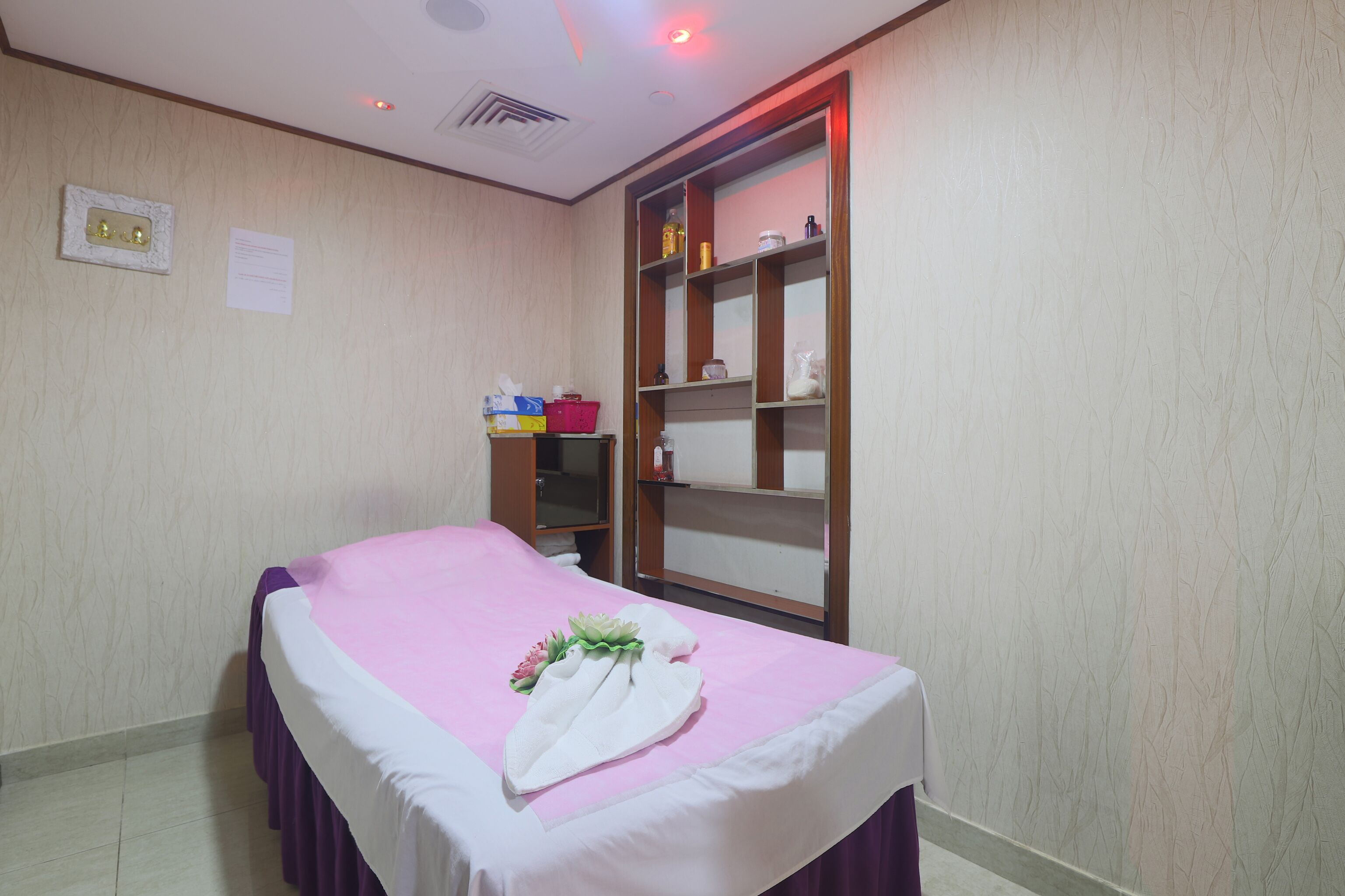A neatly arranged room with a bed, a shelf with toiletries, and a wall-mounted light fixture.