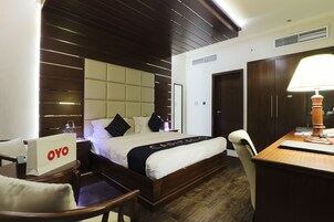 A hotel room with a bed, a desk, a chair, a wardrobe, and a bedside table.