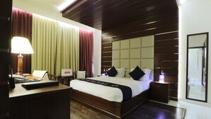 A hotel room with a wooden bed, a desk with a lamp, a nightstand, and a large mirror. - Queen Palace Hotel (Abu Dhabi)