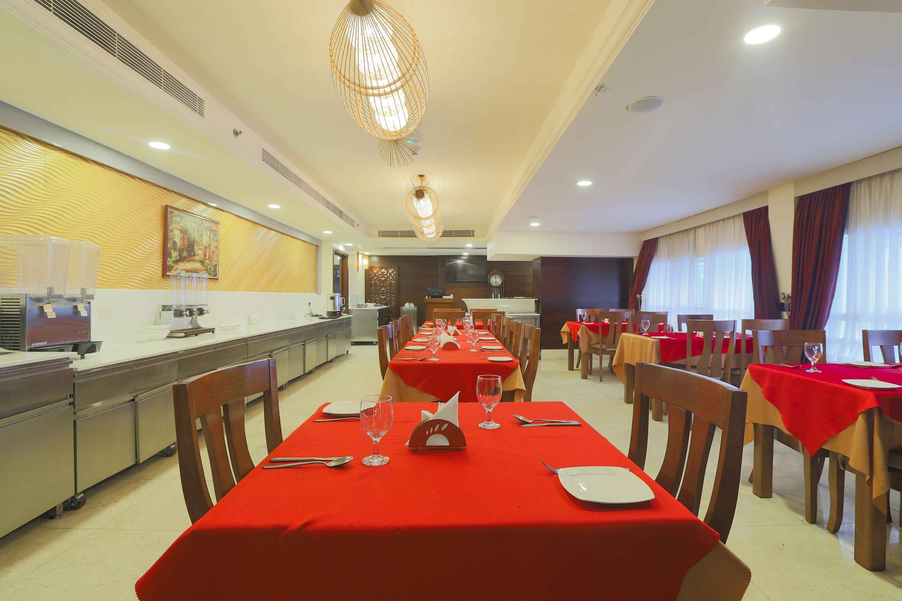 A dining area with red tablecloths, wooden chairs, and a long table with glasses and cutlery.