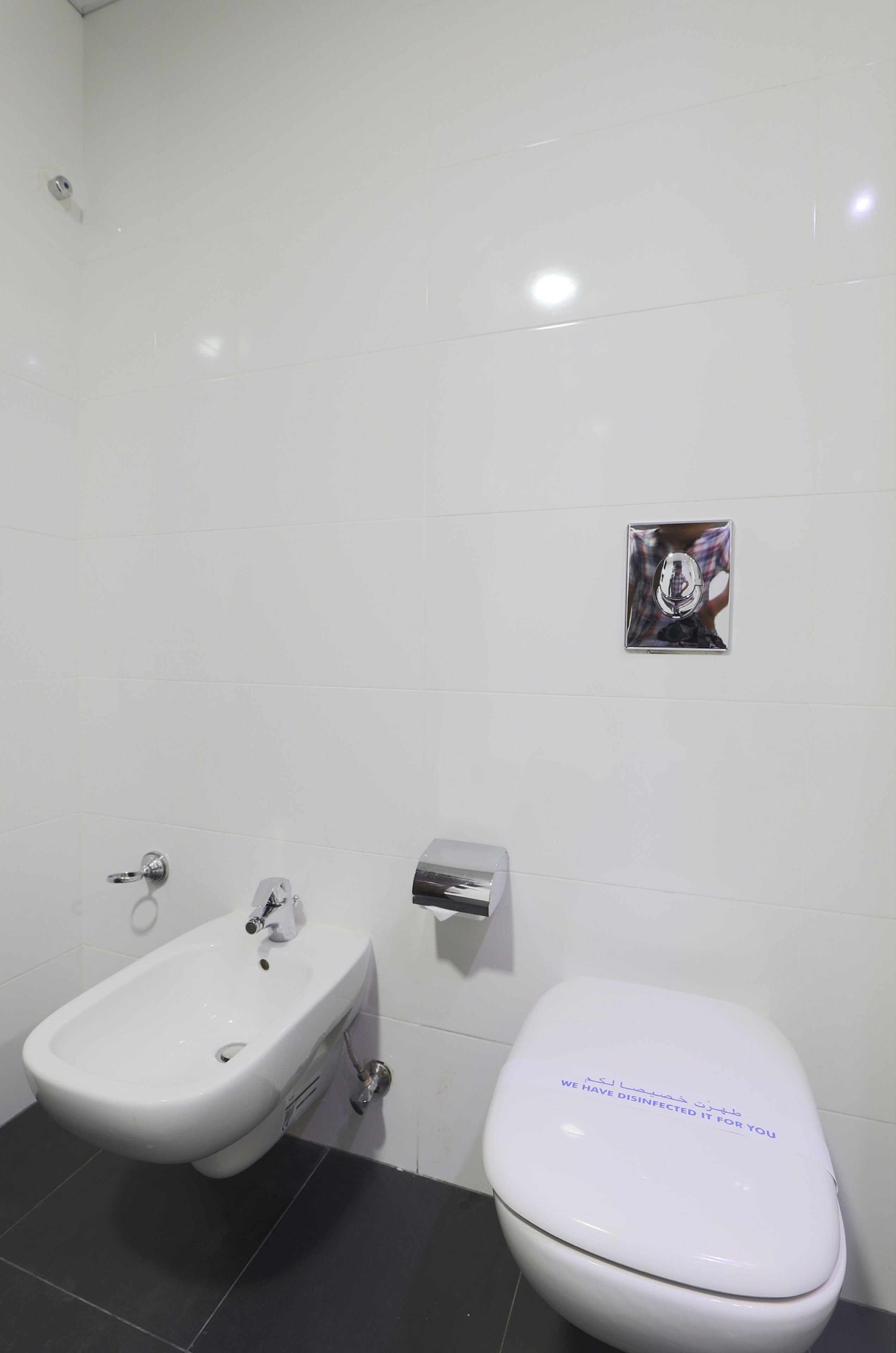 A bathroom with a white toilet, a bidet, and a hand dryer on the wall.