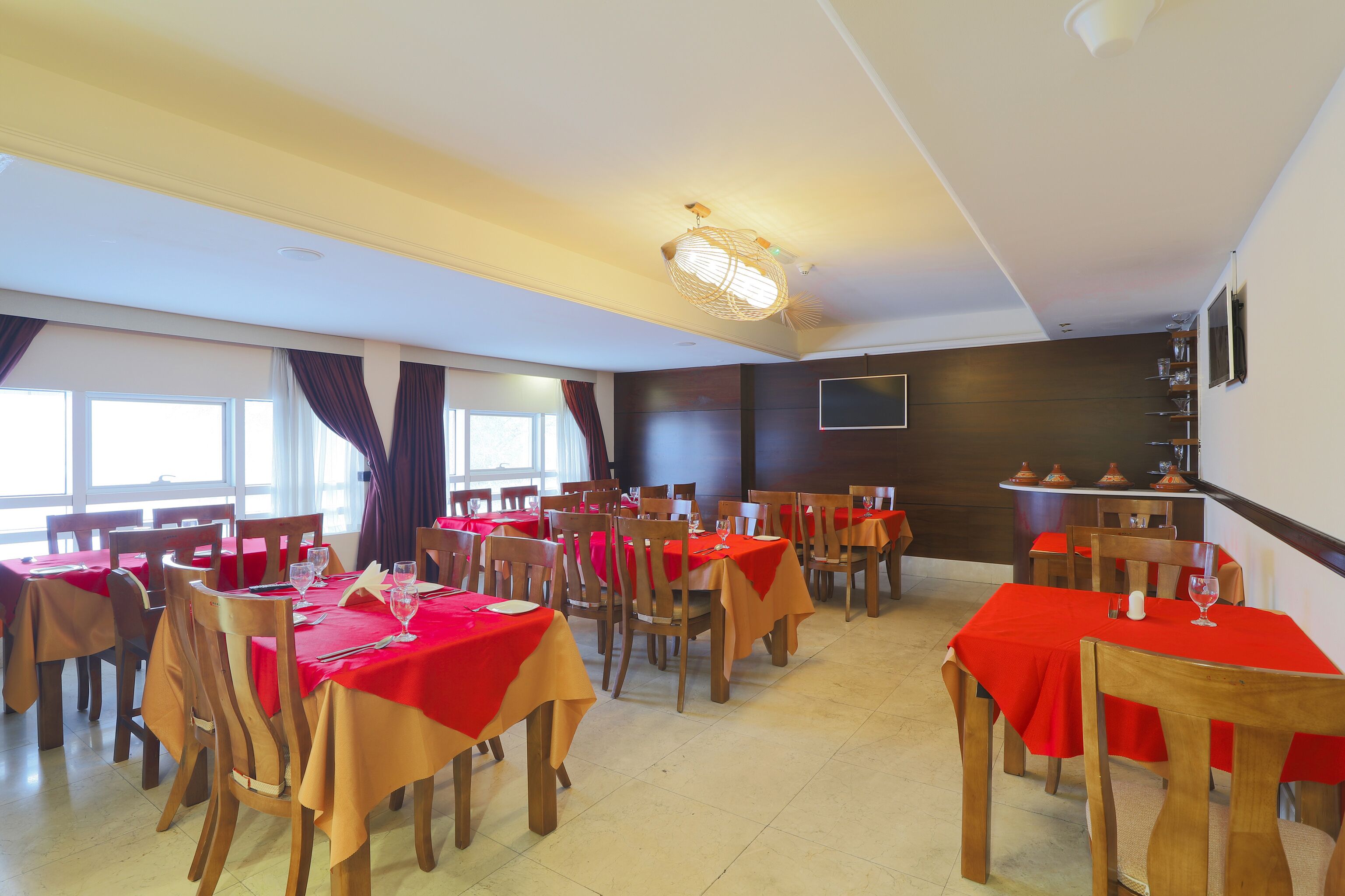A dining area with multiple tables and chairs, each covered with a red tablecloth.