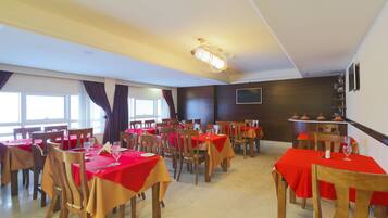 A dining area with multiple tables and chairs, each covered with a red tablecloth.