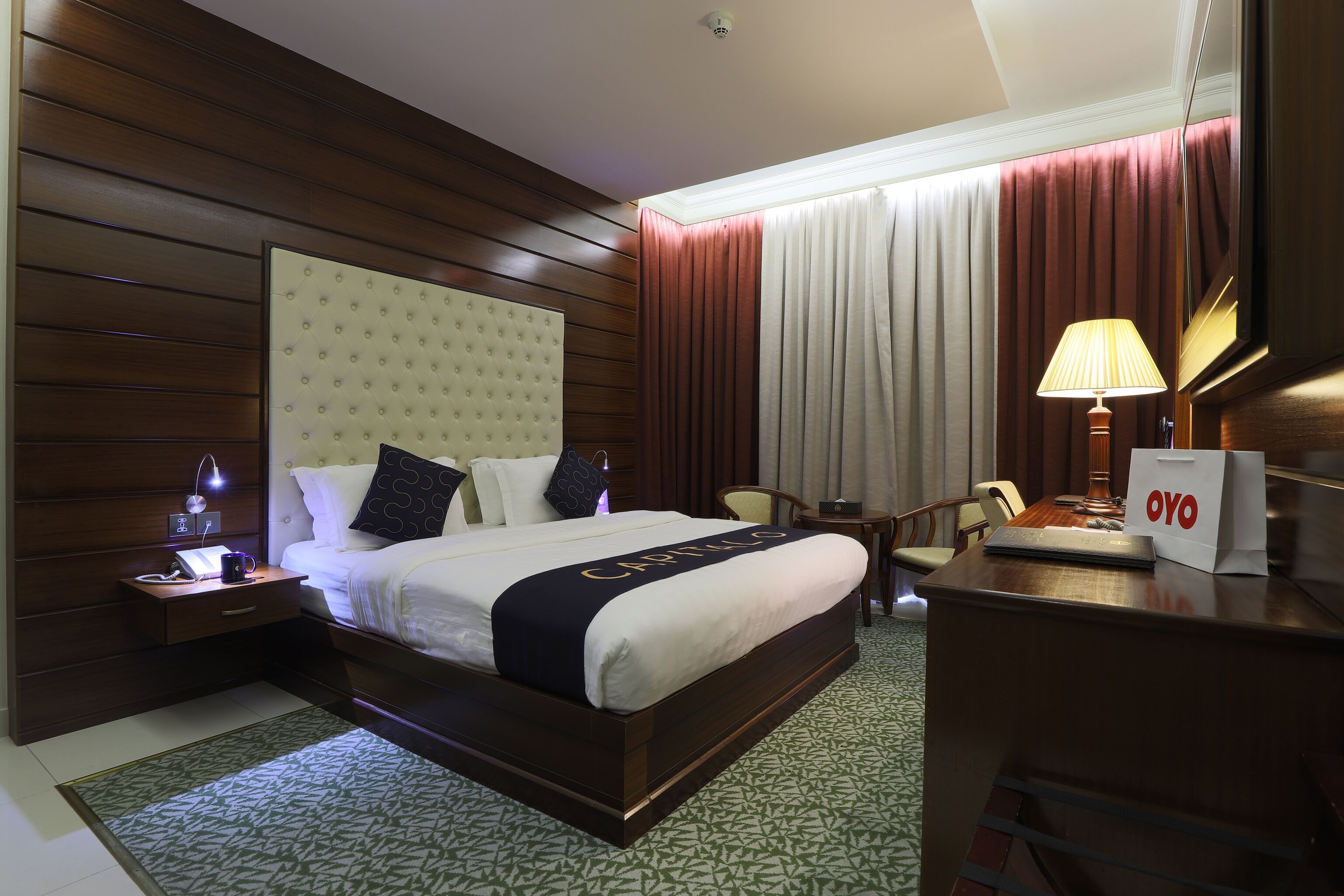 Ein Hotelzimmer mit einem großen Bett, einem Schreibtisch mit Lampe, einem Sessel und einem kleinen Tisch mit Telefon und Tasche.