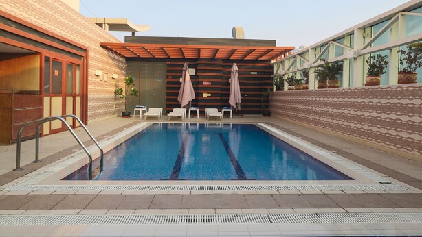 A swimming pool with lounge chairs and umbrellas, surrounded by patterned walls and a covered seating area. - Queen Palace Hotel (Abu Dhabi)