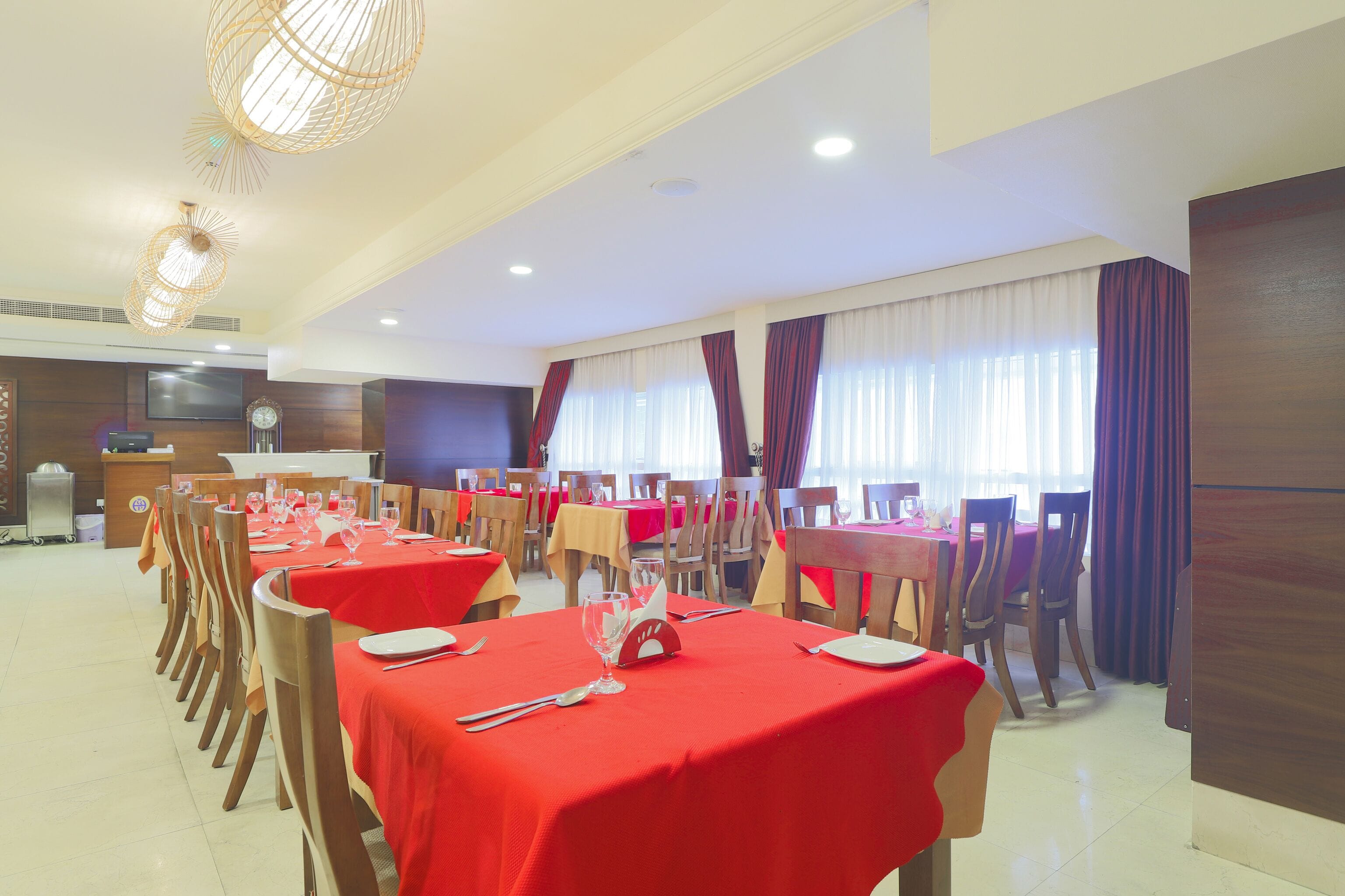 A dining area with multiple tables set for service, wooden chairs, and a clock on the wall.
