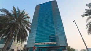 A tall, modern hotel with a glass facade and a sign in Arabic. - Queen Palace Hotel (Abu Dhabi)