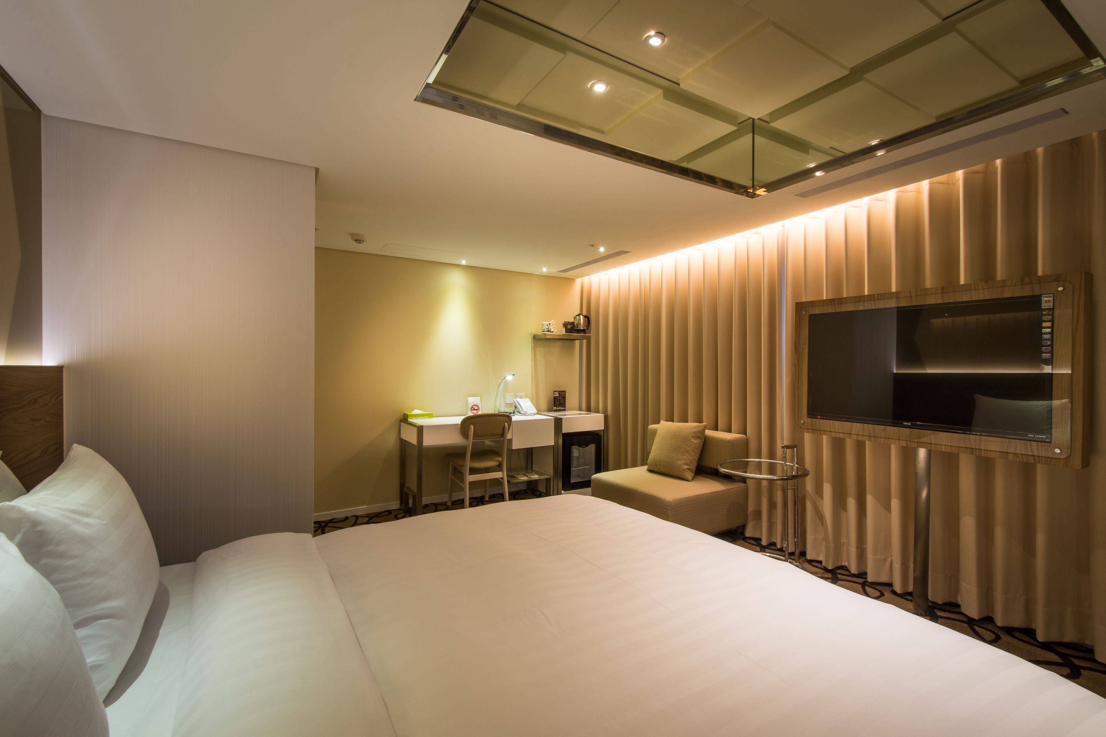 Una habitación de hotel con una cama grande, un escritorio con silla, una mesita y un televisor montado en la pared.
