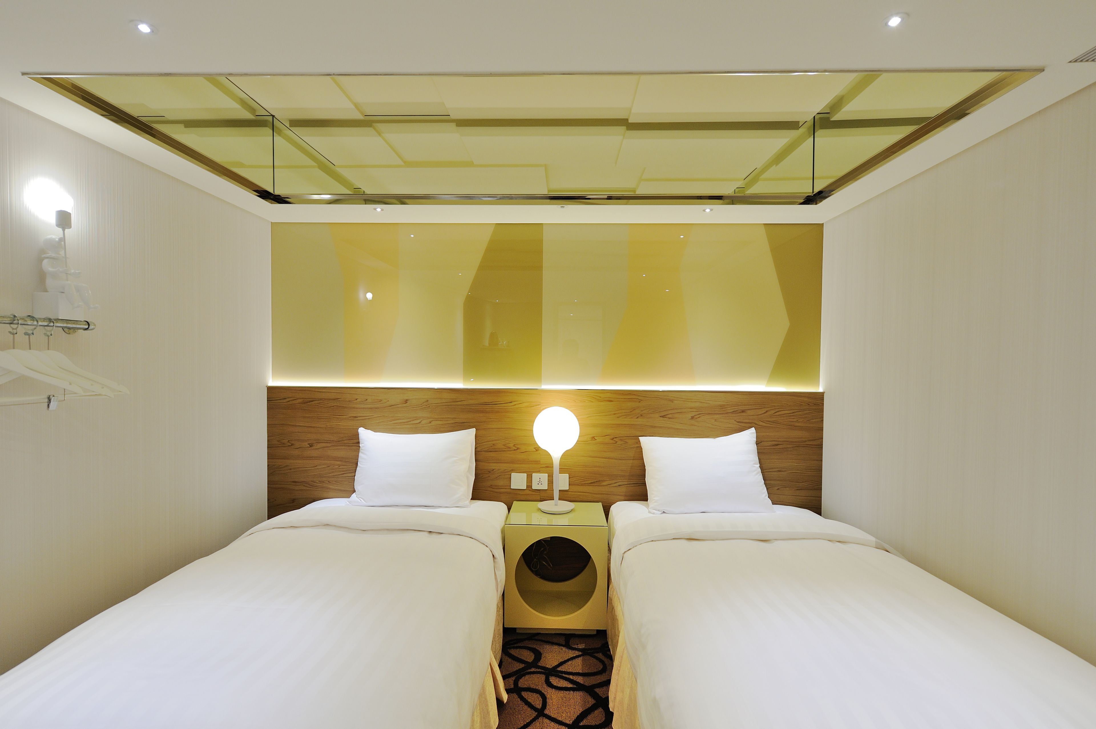 Una habitación de hotel moderna con dos camas, cabecero de madera y un diseño de techo único.