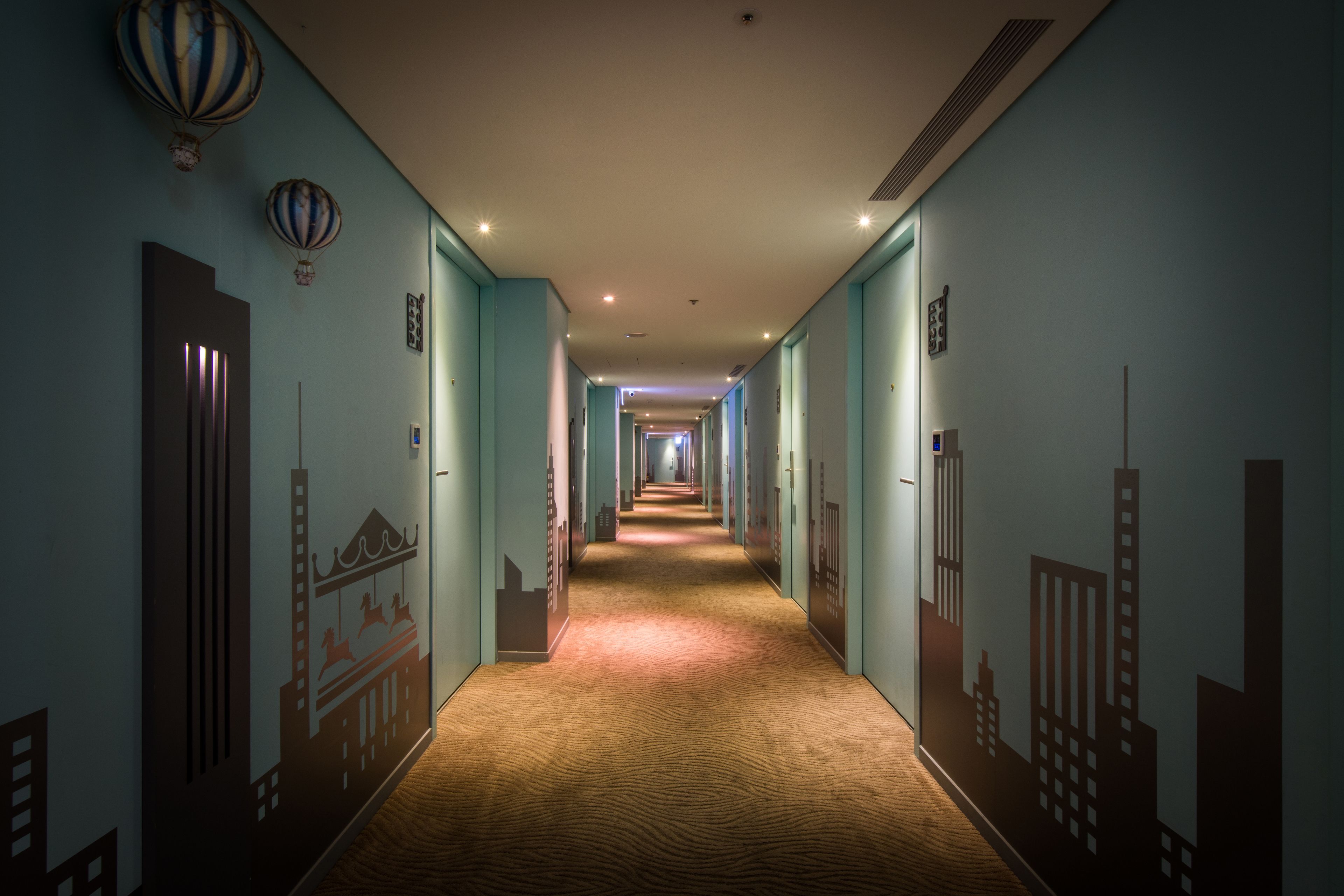 A hotel hallway with a carpeted floor, light blue walls, and a cityscape mural.