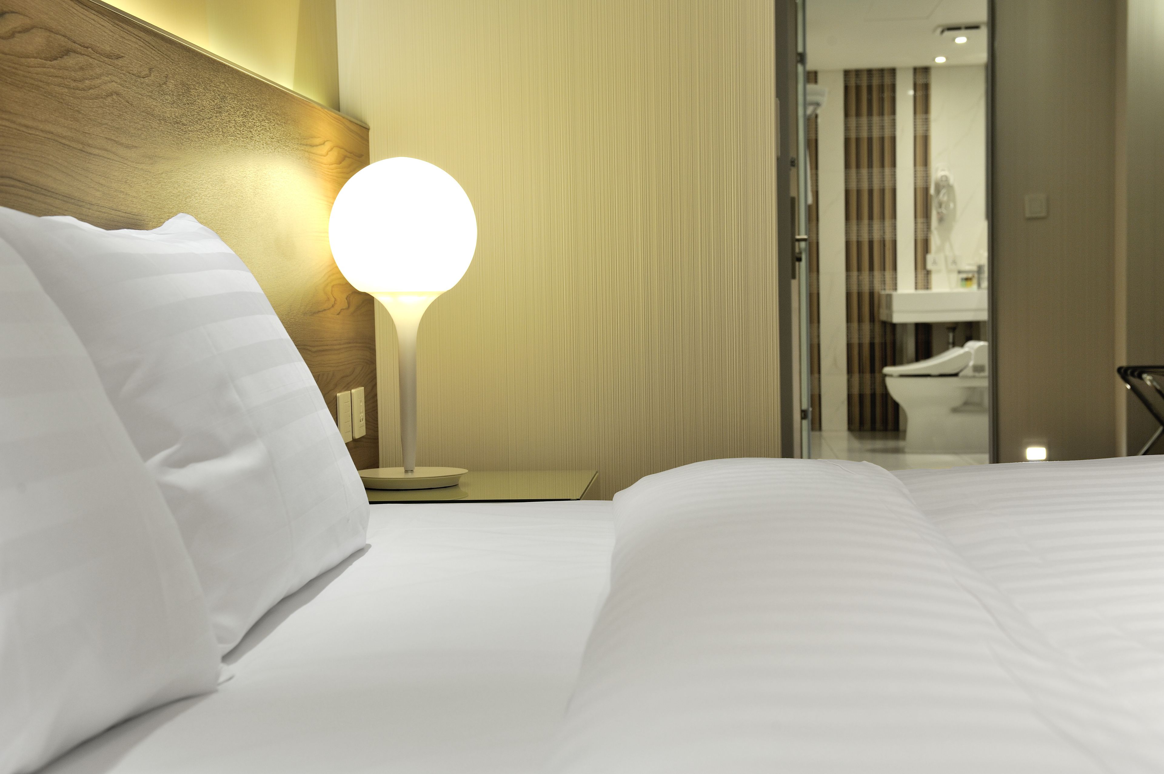 Ein Hotelzimmer mit einem ordentlich bezogenen Bett, einer Nachttischlampe und Blick ins Badezimmer.