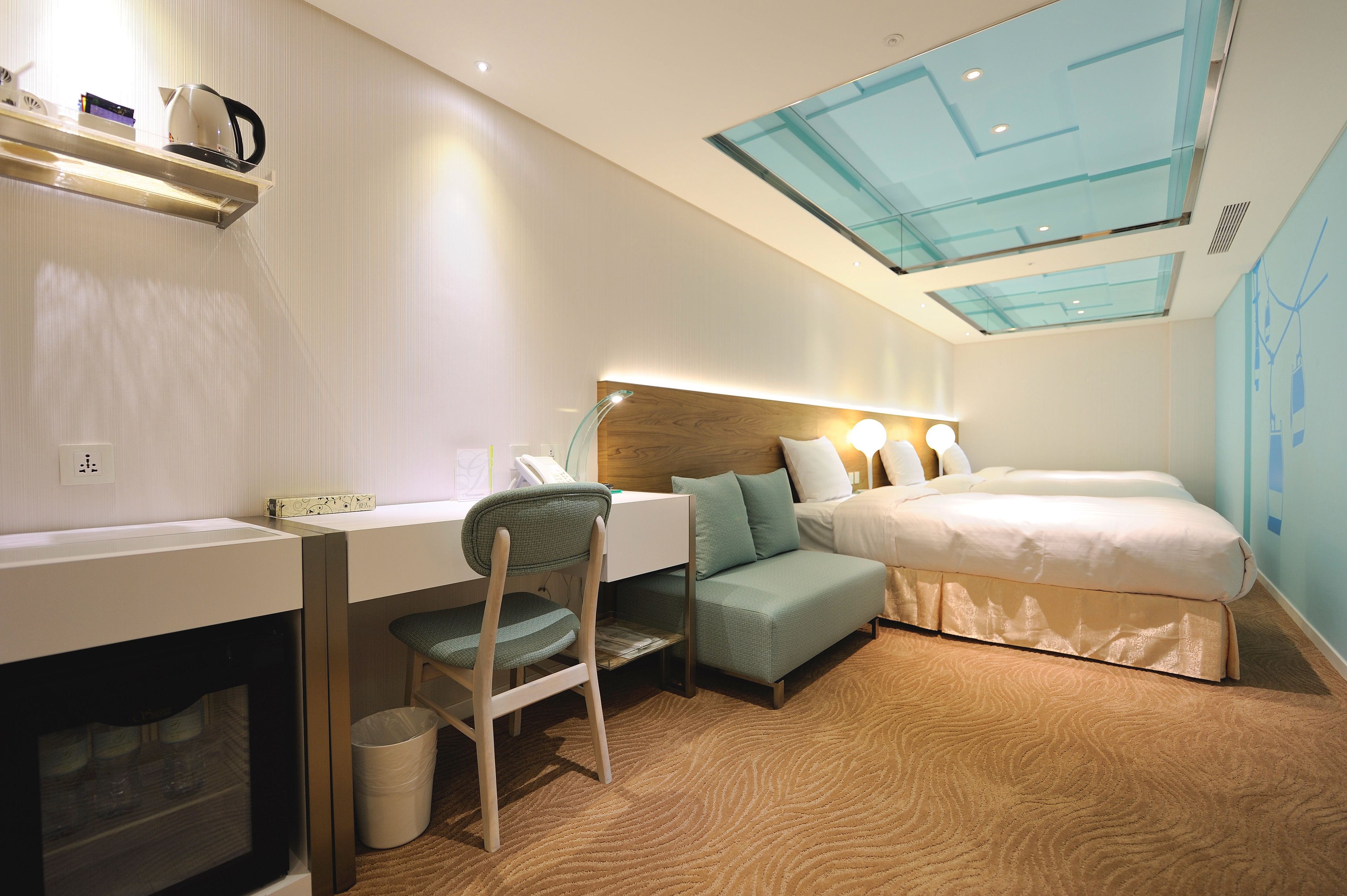 A compact hotel room with a desk, chair, and a bed with a headboard.